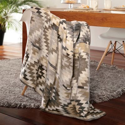 Nomad Nature filt draperad över en stol i vardagsrum, med grafiskt mönster i harmoniska beige, grå och bruna toner.