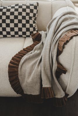 Velora rost duk med ljus väv och rostfärgad volang draperad över soffarmstöd