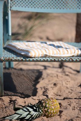Gul- och vitrandig sittdyna placerad på en turkos metallstol på sandstrand