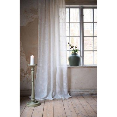 Desire offwhite skir gardin i linnemix med broderade blomslingor. Den ljusa gardinen faller mjukt framför ett fönster och släpper igenom dagsljus för en luftig och romantisk känsla.