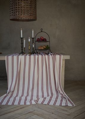 Hedvig offwhite bordsduk 140x280 cm med röda broderade ränder, draperad över ett träbord i en rustik dukning med ljusstakar och serveringsfat.