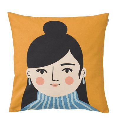 Kuddfodral från Spira med motivet Jasmine – en leende kvinna med svart hår i knut, blå polokrage och senapsgul bakgrund.