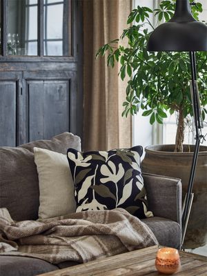 Belinda kuddfodral med svart, cremefärgad och olivgrön brodyr placerat i en brun soffa i en ombonad vardagsrumsmiljö.
