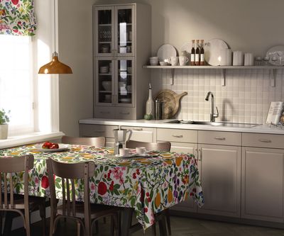 Williamspäron multi bordsduk på ett matbord i ett ljust kök med matchande hissgardin och ett färgrikt mönster av frukt, bär och blommande grenar.
