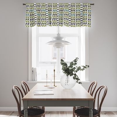 Bladiblad grön gardinkappa med retroinspirerat bladmönster upphängd i ett ljust fönster ovanför en matplats.