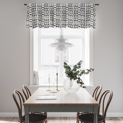 Bladiblad blå gardinkappa med retroinspirerat bladmönster upphängd i ett ljust fönster ovanför ett matbord.