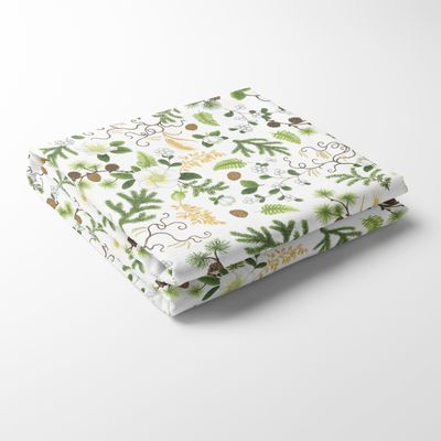 Närbild på den vikta bordsduken Barr & Blom med grönskande barr, vita blommor och små kottar på vit bakgrund.