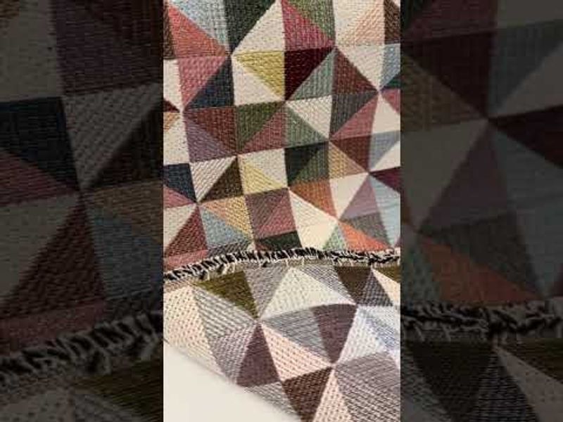Multifärgat gobelängtyg med färgglada trianglar, idealiskt för att addera en geometrisk och färgstark touch till möbler och textilier.