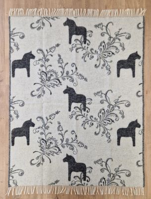 En super mysig pläd med mönstret kurbits och dalahästar, grå och offwhite från Arvidssons Textil