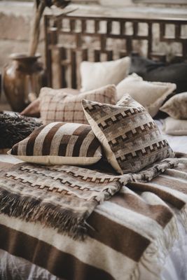 Angeline pläd i ull och silke tillsammans med matchande mönstrade kuddar i bruna och naturfärger på säng