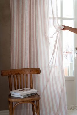 Disa gardin upphängd framför fönster med ljusinsläpp, synlig trästol och böcker i förgrunden