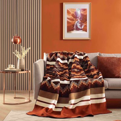 Nomad Spirit filt draperad över en ljus soffa i ett varmt inrett vardagsrum med roströda och bruna detaljer.