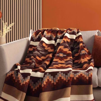 Nomad Spirit filt över en ljus soffa med etnoinspirerat mönster och blockränder i rostrött, mörkbrunt, beige och ecru.