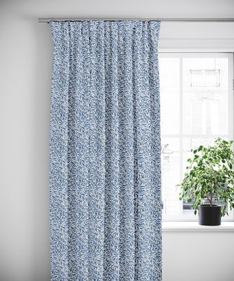 Blå mönstrade gardiner upphängda i ett ljust rum med ett fönster och blomkruka.