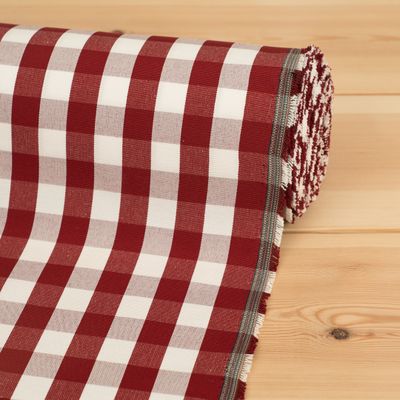 Rullad röd och offwhite rutig tyg på en träyta, med en robust vävning lämplig för tapetsering av möbler eller som gardintyg.