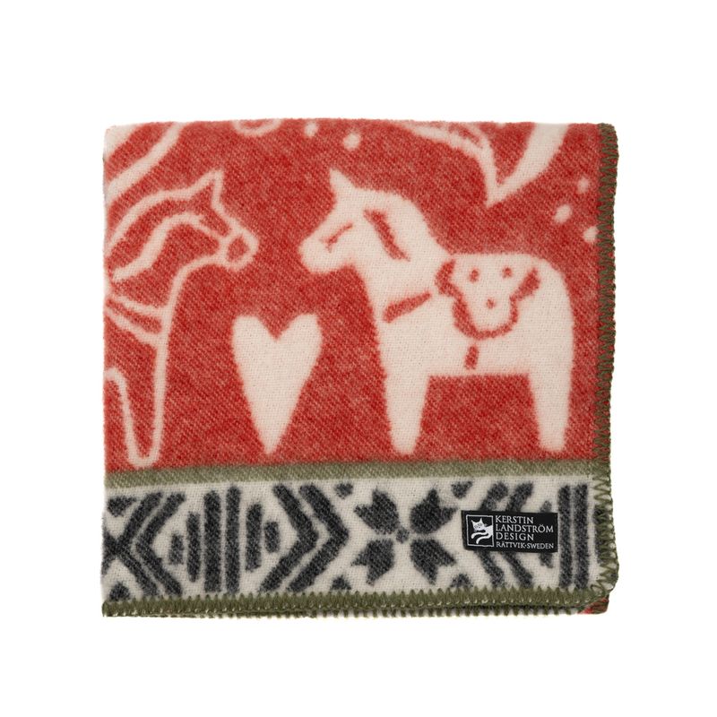 Röd barnfilt med dalahäst- och kurbitsmotiv, omgivet av traditionella dräktbandsmönster, från DALARNA serien.
