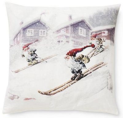 Kuddfodral med vintrigt motiv där tre tomtar åker skidor i ett snöigt fjällandskap framför röda stugor.
