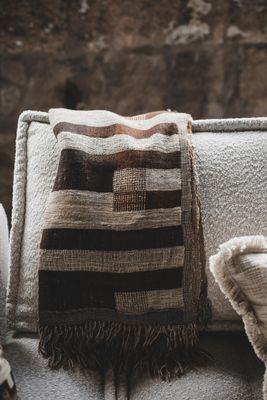 Angeline pläd i bruna och naturtoner med fransar draperad över ljus soffa i varm och rustik miljö