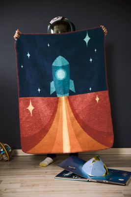 Barn håller upp Little Rocket-filten med raketmotiv och stjärnor