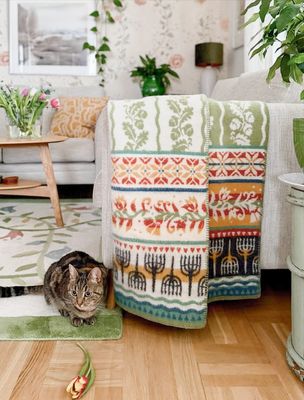 Kustland ullfilt hängande över en fåtölj i ett hemtrevligt vardagsrum, med katt på golvet och tulpan i förgrunden.