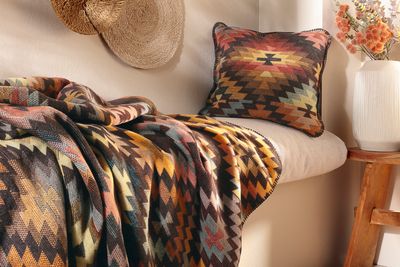 Filt med geometriskt etnomönster draperad över soffa tillsammans med kudde.