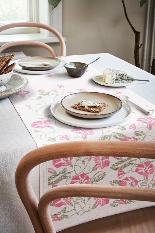 Romantisk design. 'Åkervinda' bordslöpare 35X120 cm, med ett flor av rosa blommor på vit bakgrund, svensktillverkad från ekologiska material, GOTS-märkt.