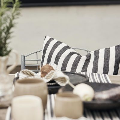 Svartvitrandigt kuddfodral i metallstol vid dukat bord med matchande randig textil.
