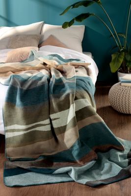 Iceland Horizon filt placerad på säng i ljus sovrumsmiljö med blå vägg