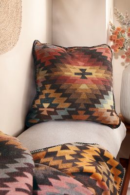 Kuddfodral i varma färger placerad i soffa med pläd