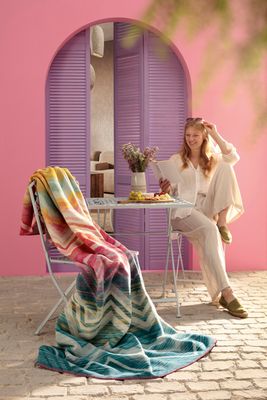 Riviera Mirage filt draperad över stol på uteplats i färgstark och solig miljö