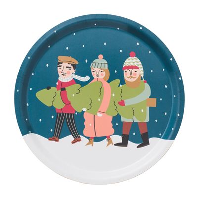 Rund bricka med vintermotiv av tre personer som bär en julgran i snöväder, mot blå bakgrund.