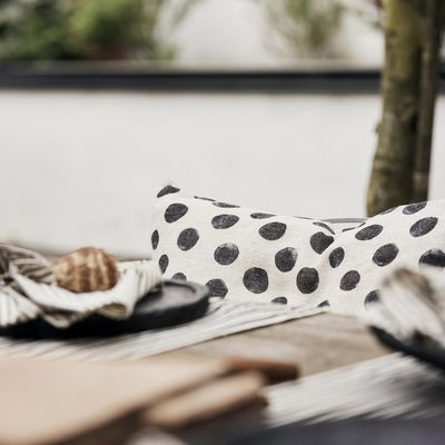 Svartprickigt kuddfodral placerat i stol vid dukat bord med randiga textilier.