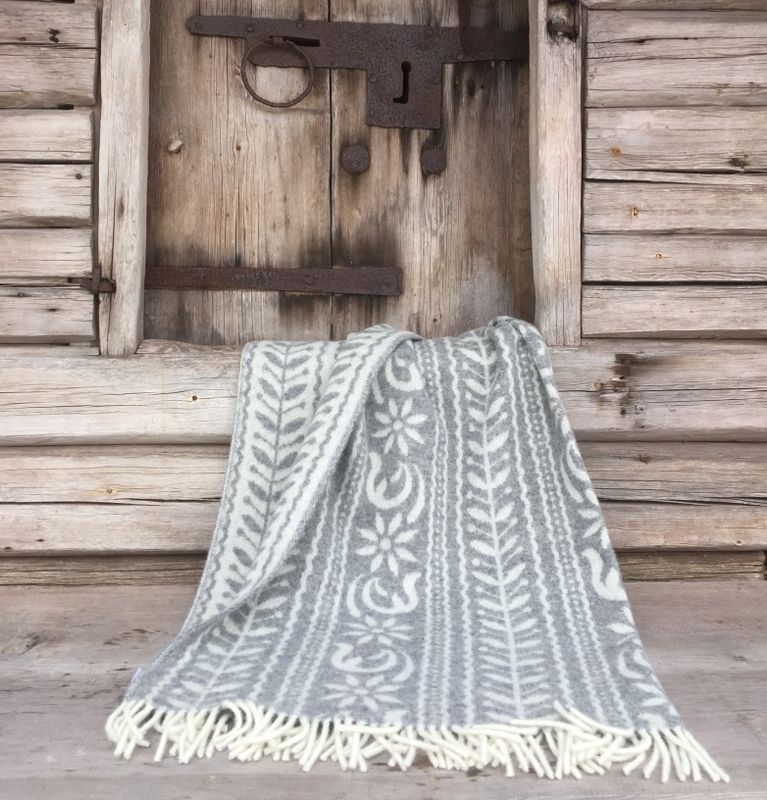 ANNO 1862 grå och vit ullpläd draperad över en bänk, med fina fransar och ett traditionellt mönster, symboliserar svensk hantverkskultur.