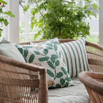 Miljöbild med Renfana grön kuddfodral från Spira of Sweden i en rottingsoffa med gröna och randiga kuddar i ett ljust sommarrum med stora fönster