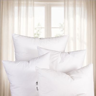 Flera vita innerkuddar placerade framför ljusa gardiner i ett hem