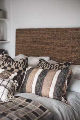 Delia kuddfodral med grafiskt rutmönster i jordnära toner placerat på säng tillsammans med matchande textilier