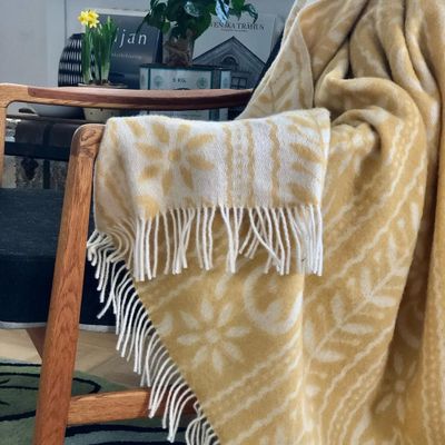 En gul och vit ANNO 1862 Ullpläd elegant draperad över en bänk, med detaljer som återspeglar svensk tradition och hantverksmässig kvalitet.