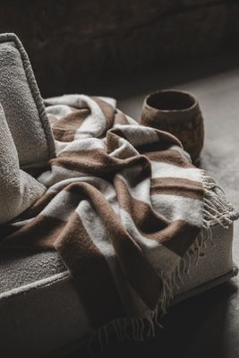 Zara Blockstripe ljusbrun pläd med breda blockränder, draperad över en soffa i varm och ombonad miljö.