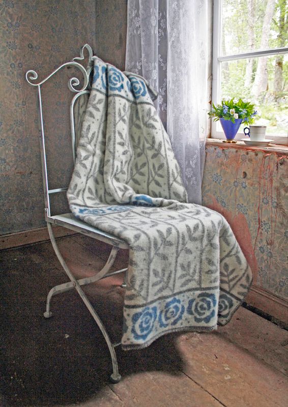Den charmiga 'Rosengård' ullfilten ligger på en antik stol bredvid ett fönster, vilket framkallar en nostalgisk och behaglig atmosfär i rummet