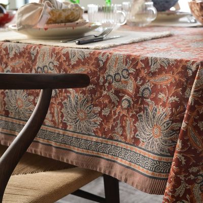 Bordduk i varma rosttoner med dekorativ bård, omgiven av glas, keramik och ljus för en ombonad känsla.