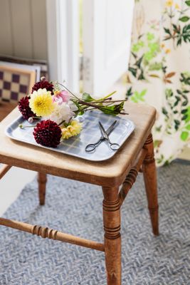 Kristina blå serveringsbricka med blomsterbukett och sax på en trästol vid ett öppet fönster.
