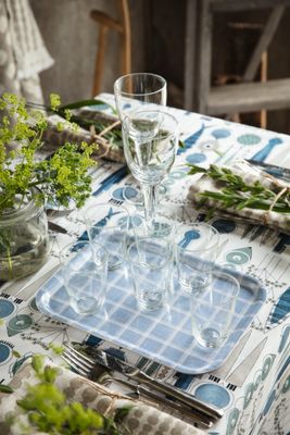 Kristina blå bricka med glas på ett dukat bord tillsammans med Picknick-mönstrad duk och sommarblommor.