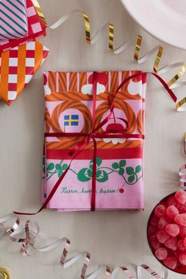 Rosa kökshandduk med kalasmotiv inslagen som present med rött sidenband.