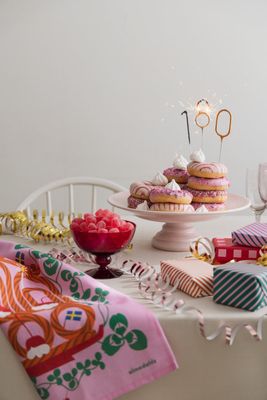 Festdukning med rosa kökshandduk, bakverk, godis och presentpaket.