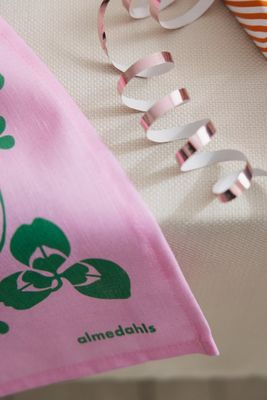 Närbild av rosa kökshandduk med Almedahls logotyp och dekorativt kalasmotiv.