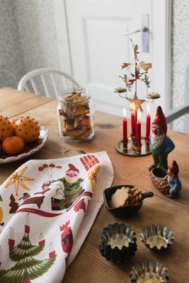 Lottas julskafferi kökshandduk från Almedahls på ett träbord med juldekorationer, pepparkakor, apelsiner och adventsljusstake.