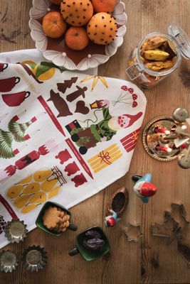Lottas julskafferi kökshandduk med tomtar, julgodis och ljusstakar på ett träbord tillsammans med apelsiner, kakor och juldekorationer.