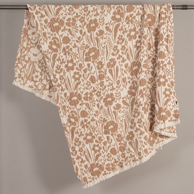 Fauna brun bomullspläd med blommönster och fransar, elegant draperad över en stång.