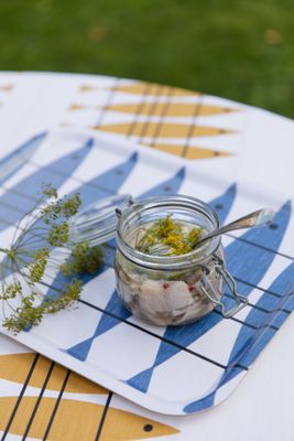 Sill blå serveringsbricka med glasburk och dukning utomhus på ett bord.