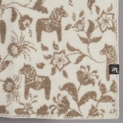 Detaljbild av beige ullpläd med dalahästar och blommönster i naturvitt